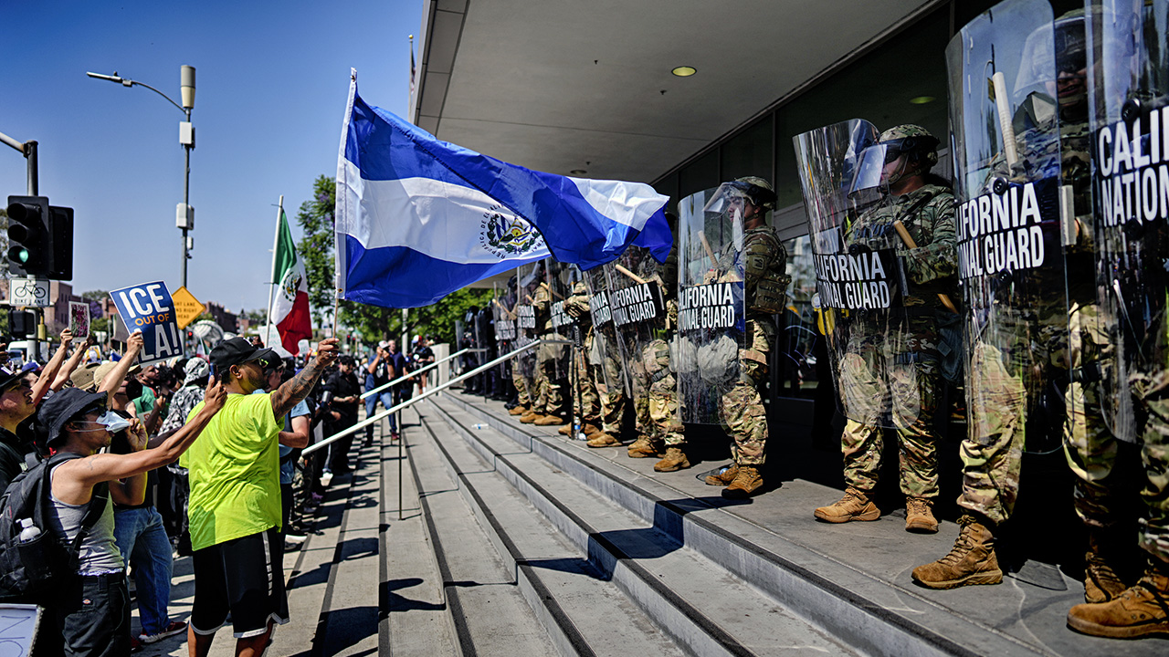 A protester waves a National Flag of El Salvador in front of a line of California National Guard in front of Federal Building on Monday, June 9, 2025, in downtown Los Angeles.